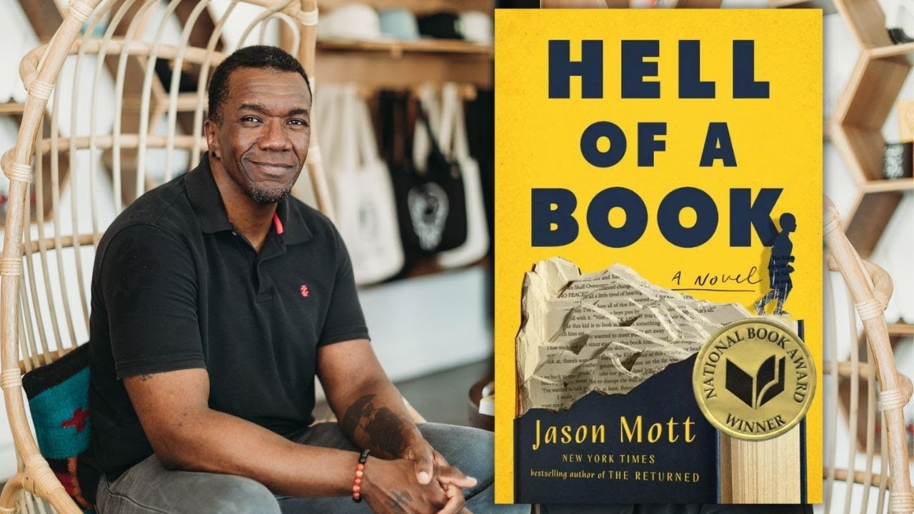 A person sitting beside the cover of the novel "Hell of a Book" by Jason Mott, indicating it's a National Book Award winner.
