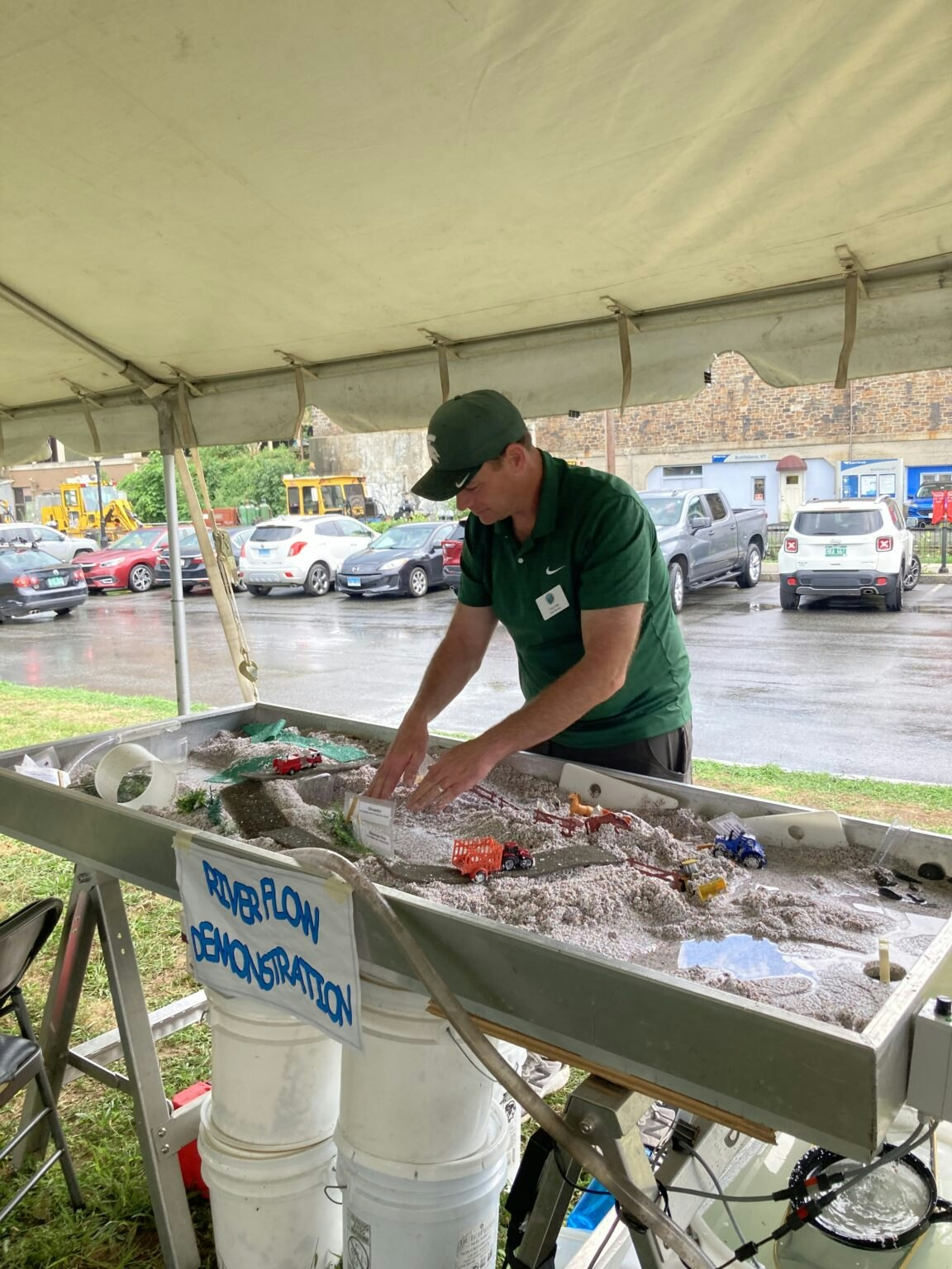 A person conducting a river flow demonstration under a canopy.