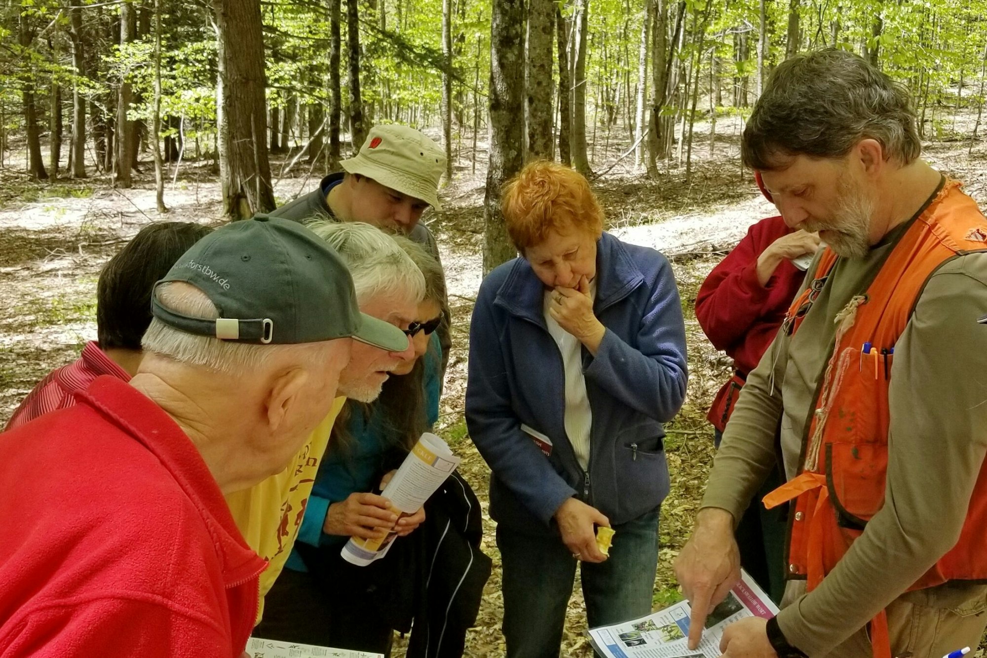 Group of people intently examining a document in a forest setting.