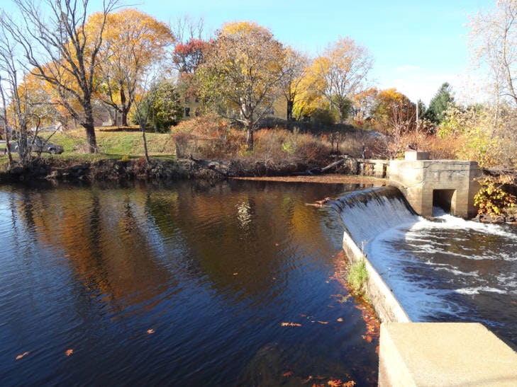 A tranquil waterfall in a river with autumn trees and a clear sky.