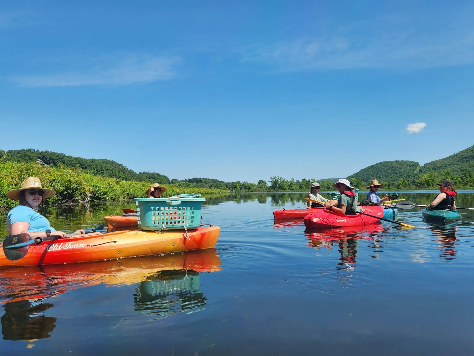 People kayaking on a calm lake, surrounded by green hills, under a clear blue sky.