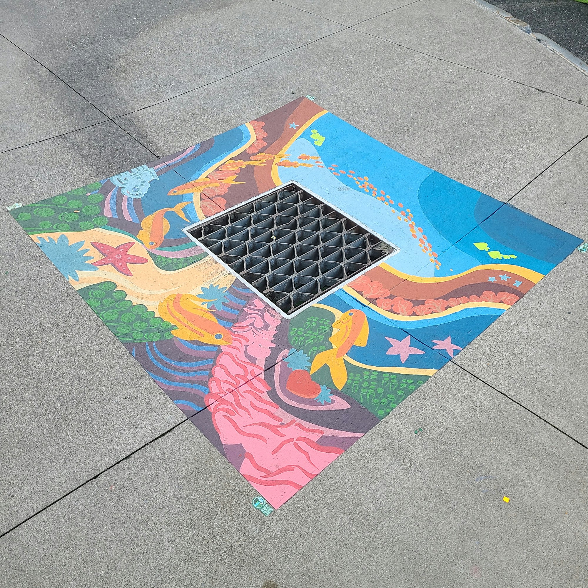 Colorful street art surrounding a storm drain on a sidewalk.