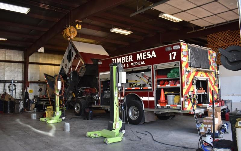 Fire truck undergoing maintenance in a garage, with equipment and tools visible around it.