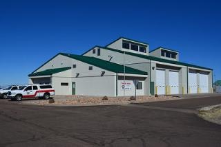 A building with multiple garage doors, a few parked vehicles outside, and a sign on the side.