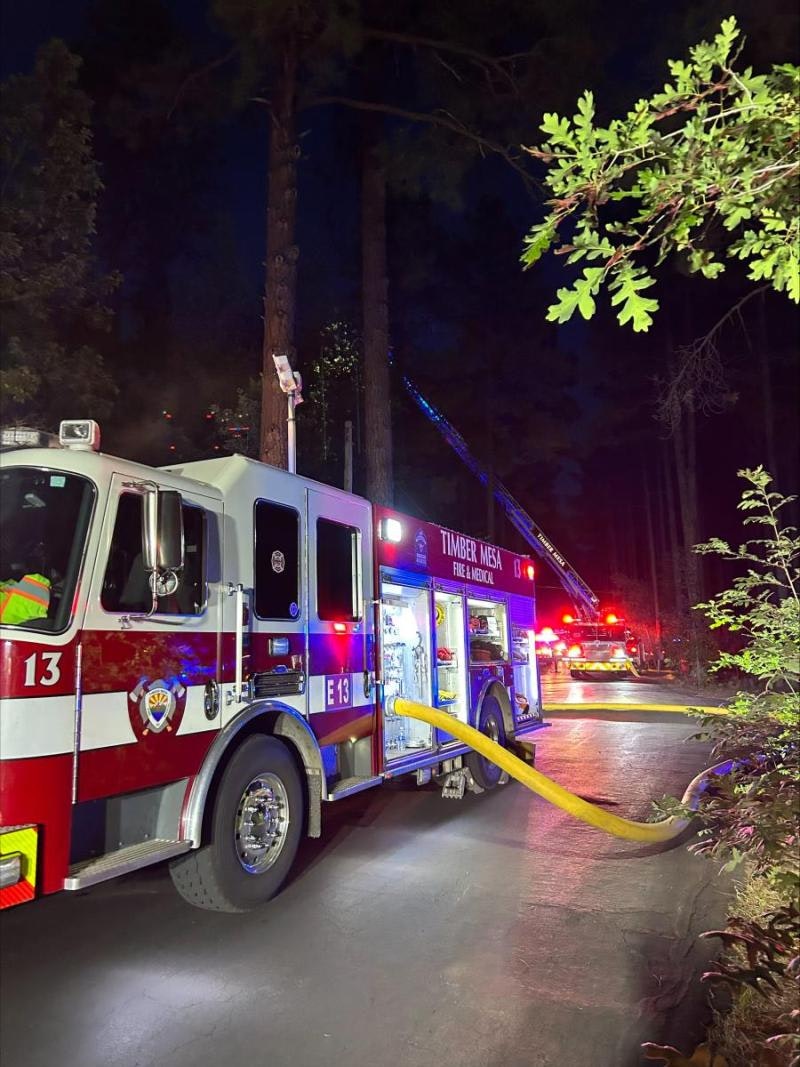 A fire truck parked on a forest road at night with a hose attached, emergency lights flashing.