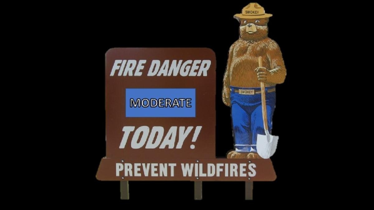 Sign with "FIRE DANGER MODERATE TODAY! PREVENT WILDFIRES" next to a cartoon bear holding a shovel.