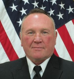 A person in a suit is posed in front of an American flag.