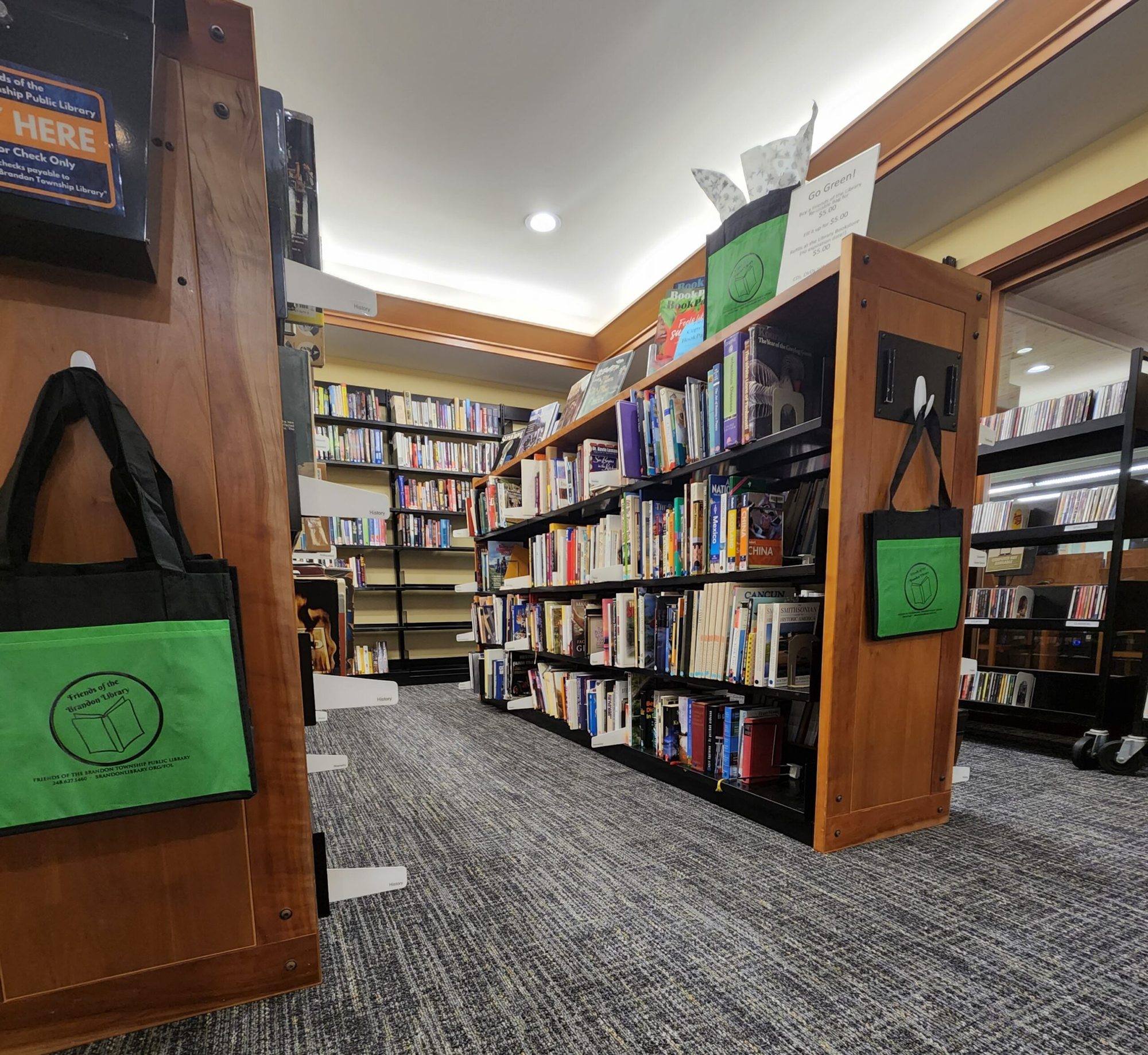 A library interior with bookshelves filled with books, green reusable bags, and a sign promoting eco-friendly practices.