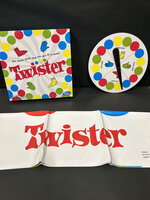Twister game set with box, color spinner, and mat featuring colored circles and "Twister" logo.