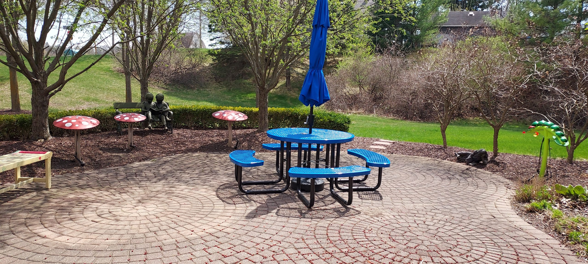 A garden scene with a blue table, mushrooms, trees, and statues of two children on a bench.