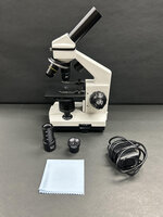 A microscope with a cleaning cloth, lens cover, and a coiled cable on a gray background.