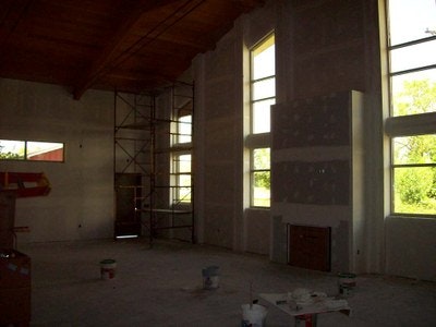 An interior under construction with drywall, a scaffold, windows, and paint supplies.