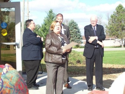 A group of people gathered outside, one woman is speaking, others are listening. It looks like a small event or ceremony.
