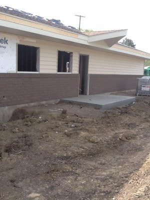 A house under construction with exposed foundation, unfinished landscaping, and building materials visible.