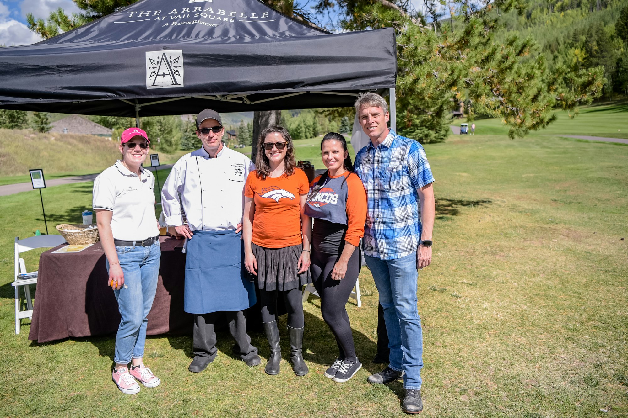 Five people posing under a tent with a sign "The Arrabelle at RockResort" outdoors on a sunny day.