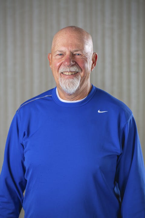 Smiling man with a beard in a blue shirt against a textured background.
