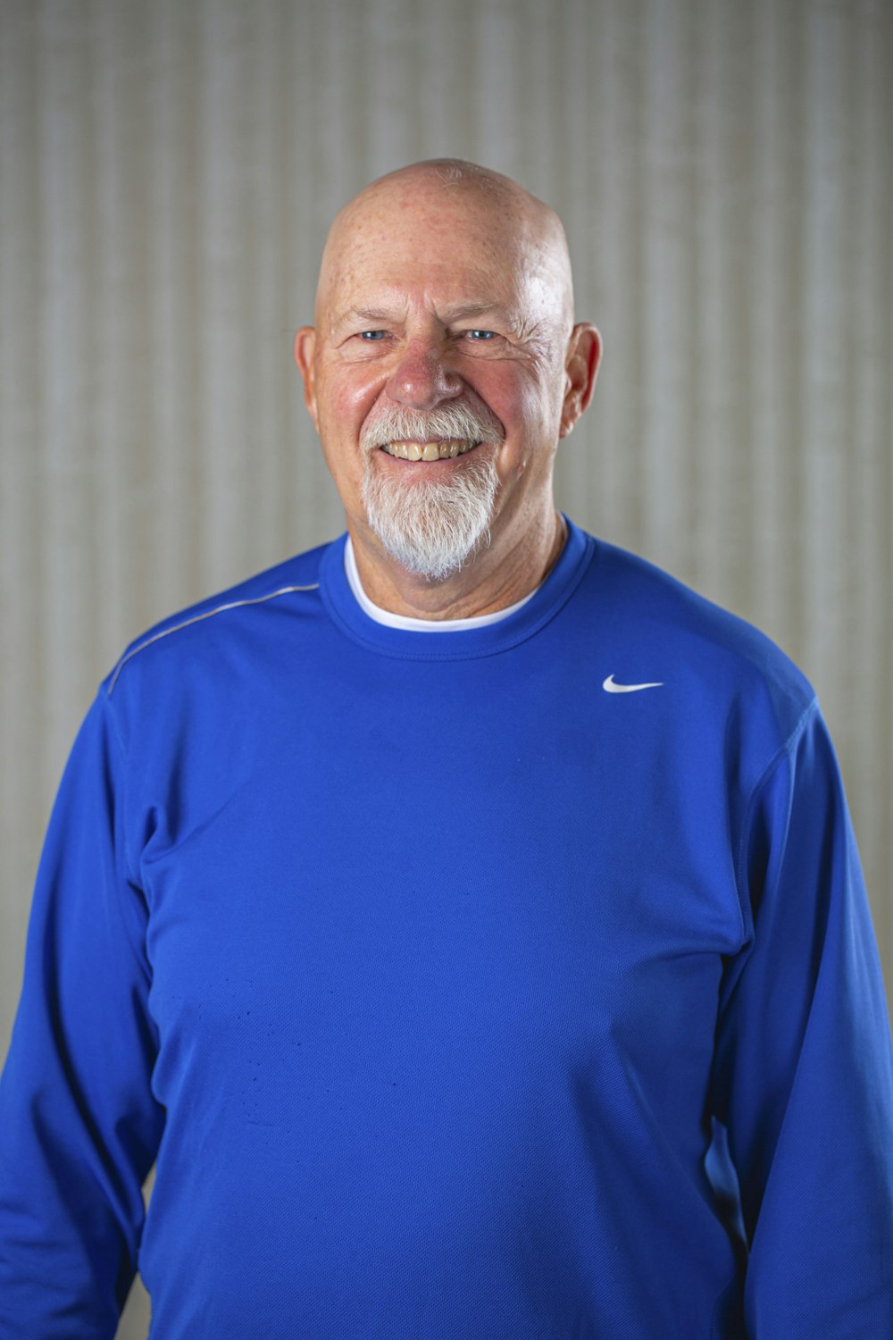 Smiling man with a beard in a blue shirt against a textured background.