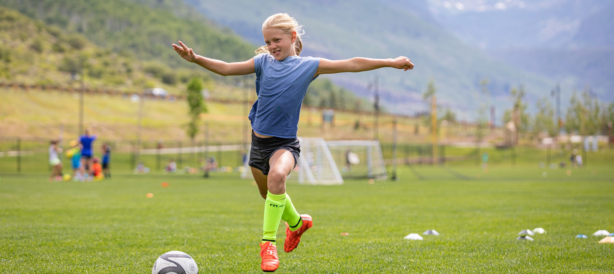 A child playing soccer on a lush field with others in the background.