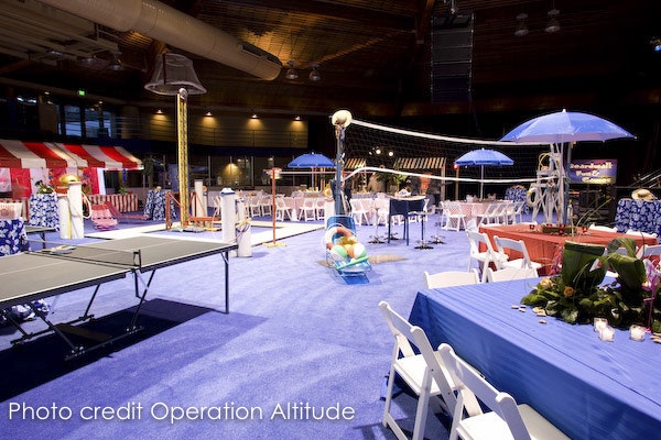 Indoor event space with beach theme, tables, umbrellas, volleyball net, and inflatable pool toy.