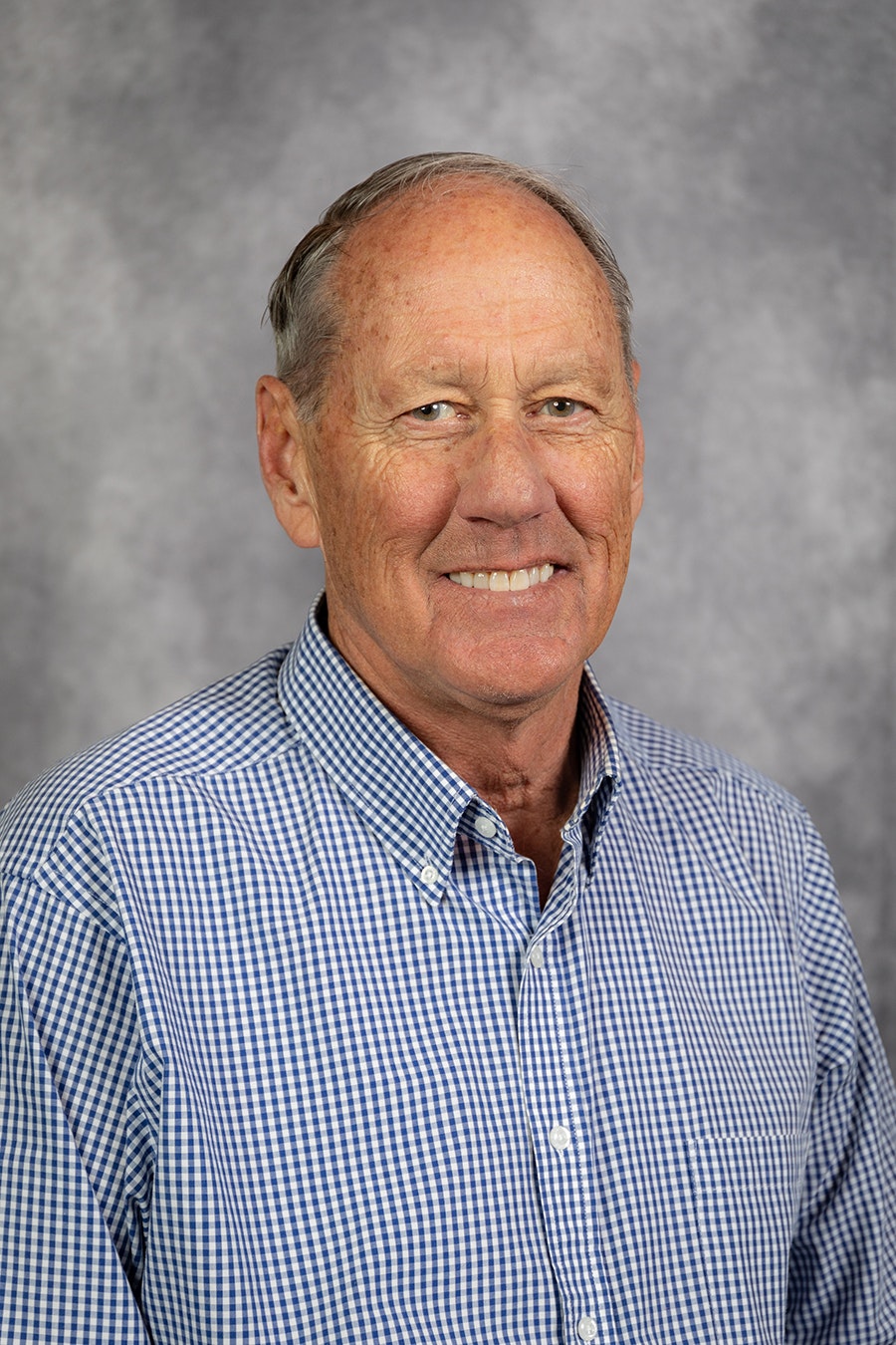 A smiling man wearing a checkered shirt, against a mottled gray background. (Photo: Professional portrait)