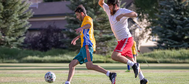 Two people playing soccer on a grass field.