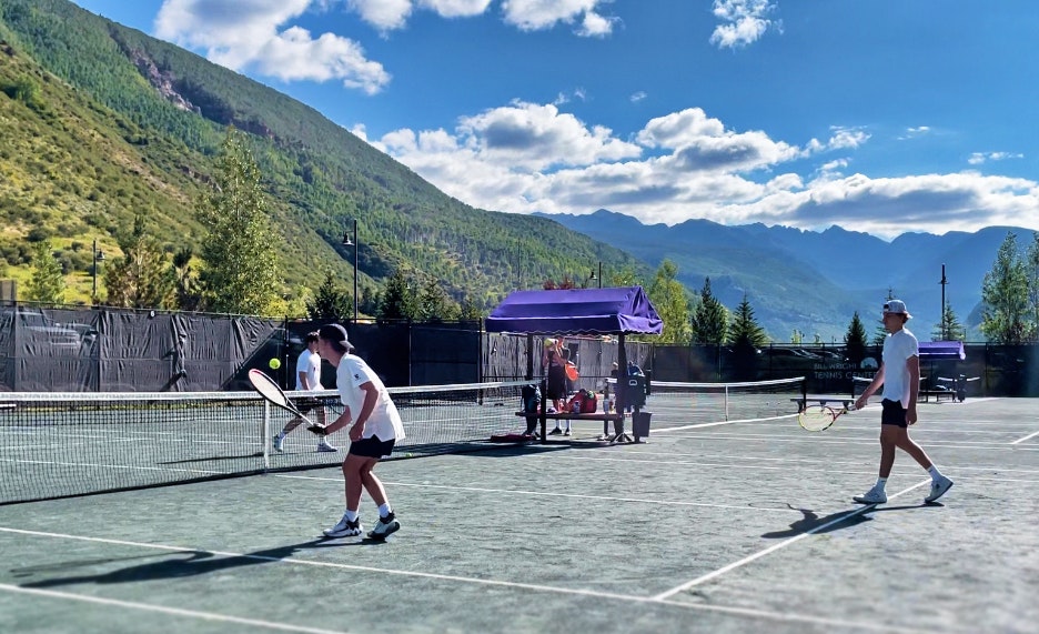 Two people playing tennis on an outdoor court with mountains in the background.
