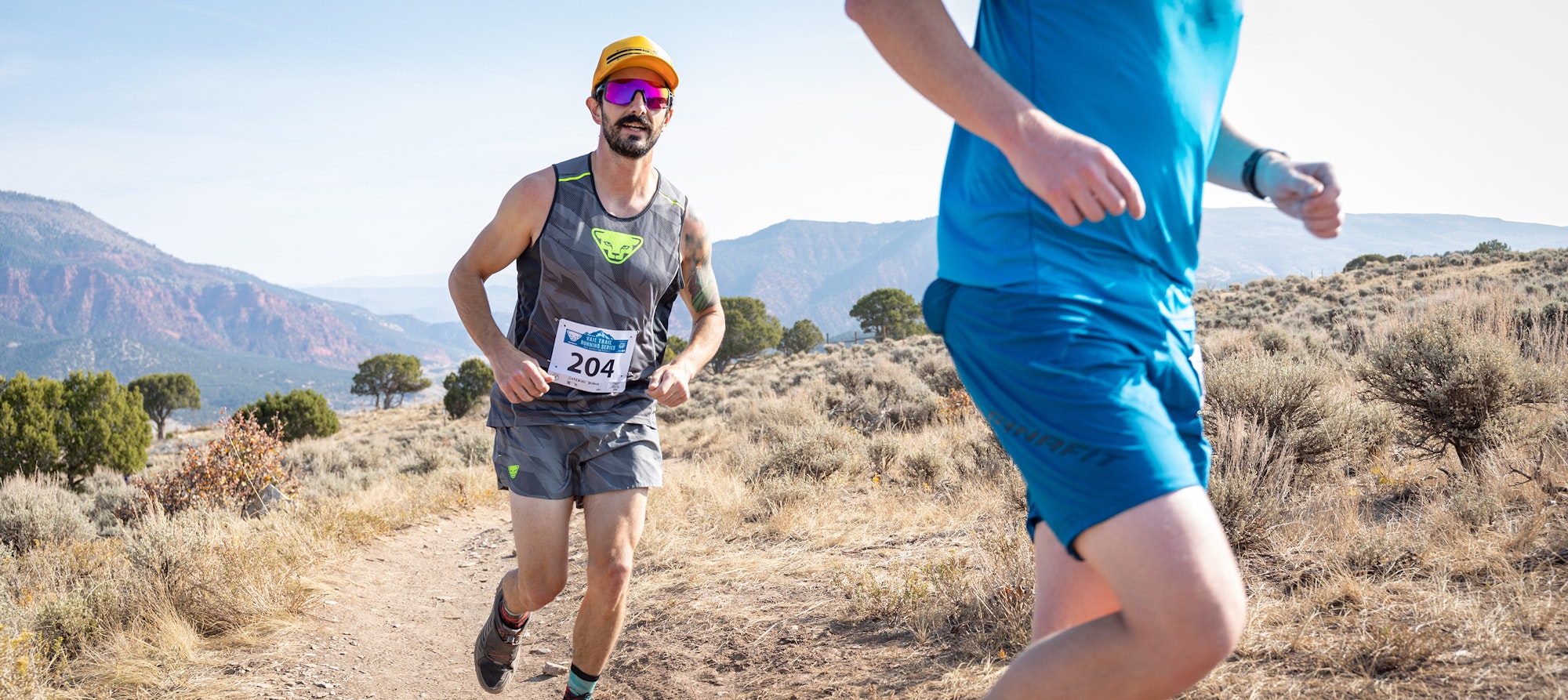 Two trail runners racing outdoors with scenic mountain background.