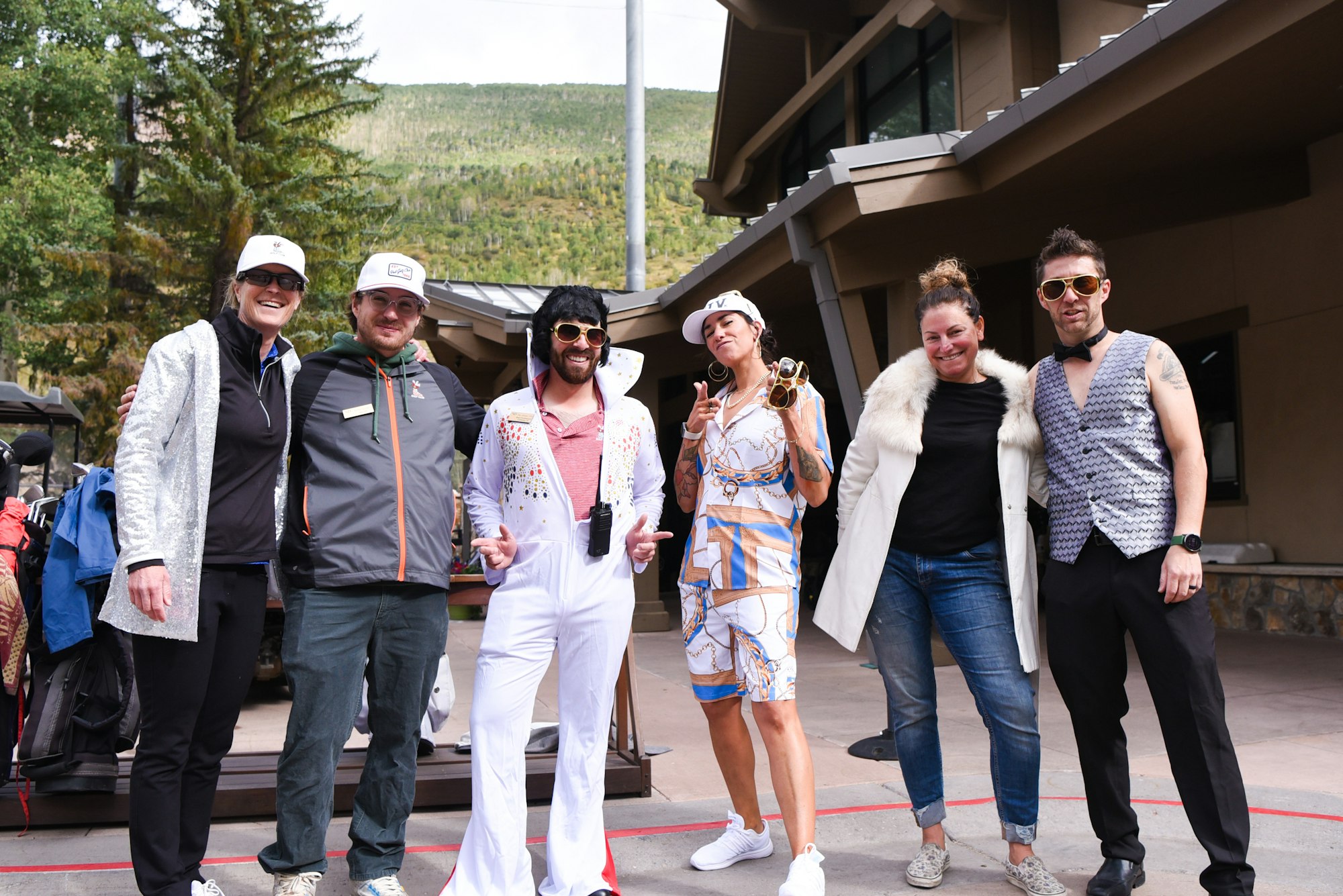 Group of people in fun costumes posing outdoors, with one dressed as Elvis.
