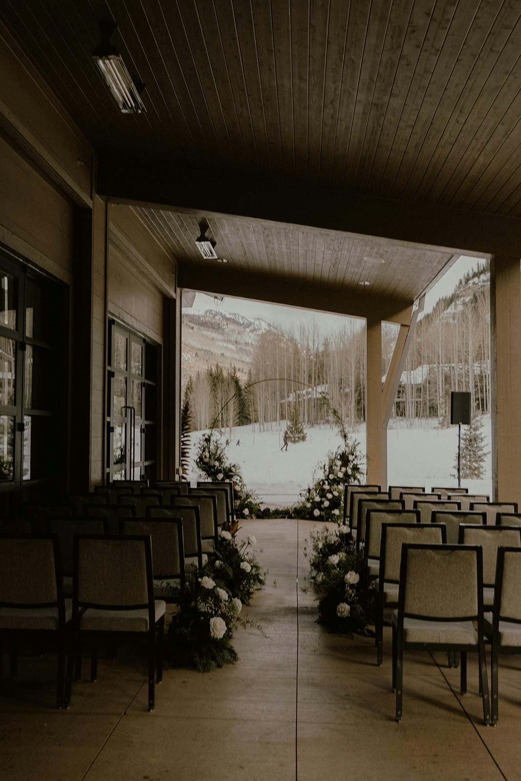 An outdoor event setup with chairs and floral decorations, overlooking a snowy landscape with bare trees and mountains.