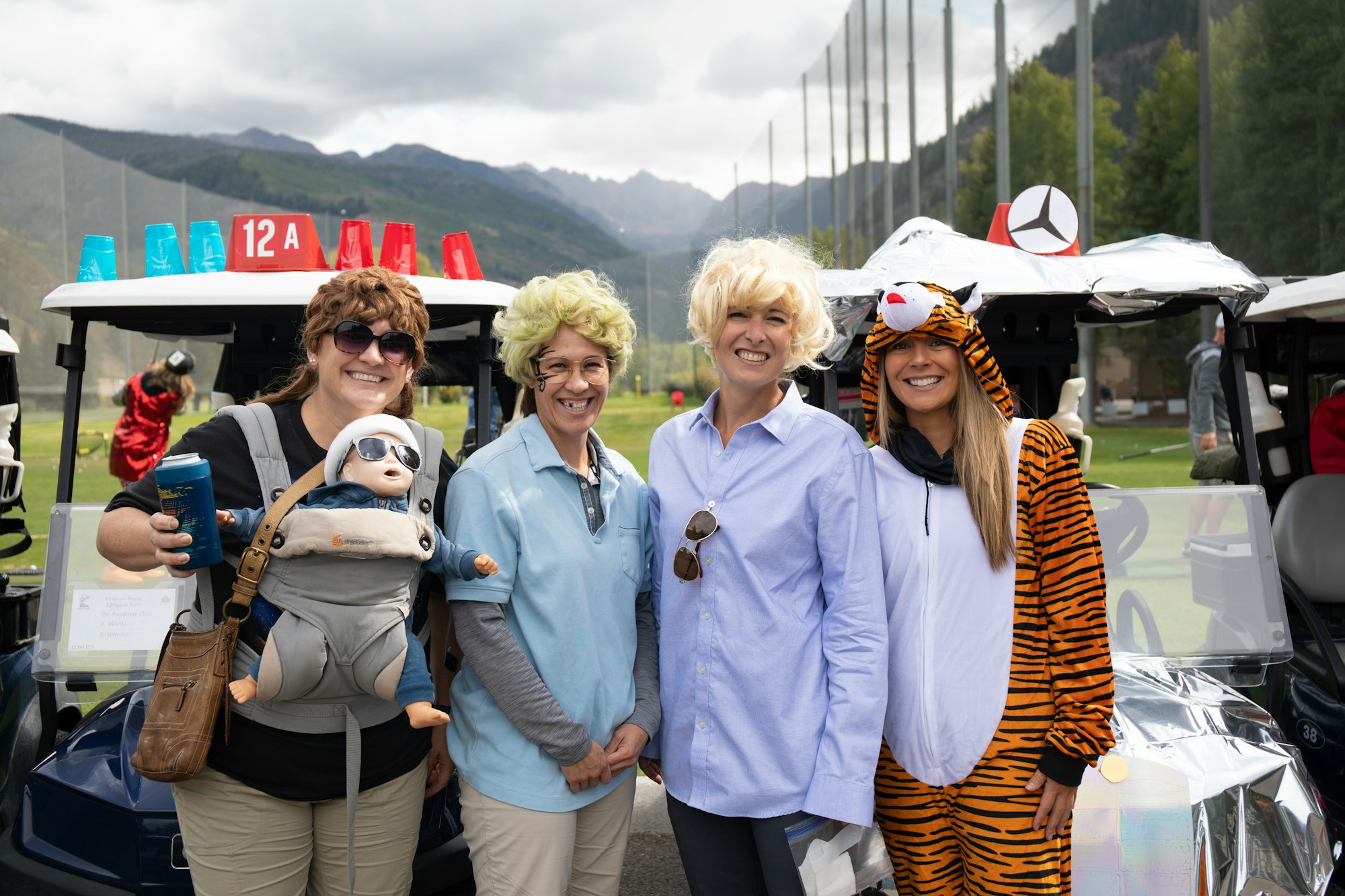 Four people in costumes with a golf cart, mountains in the background, and a playful atmosphere.