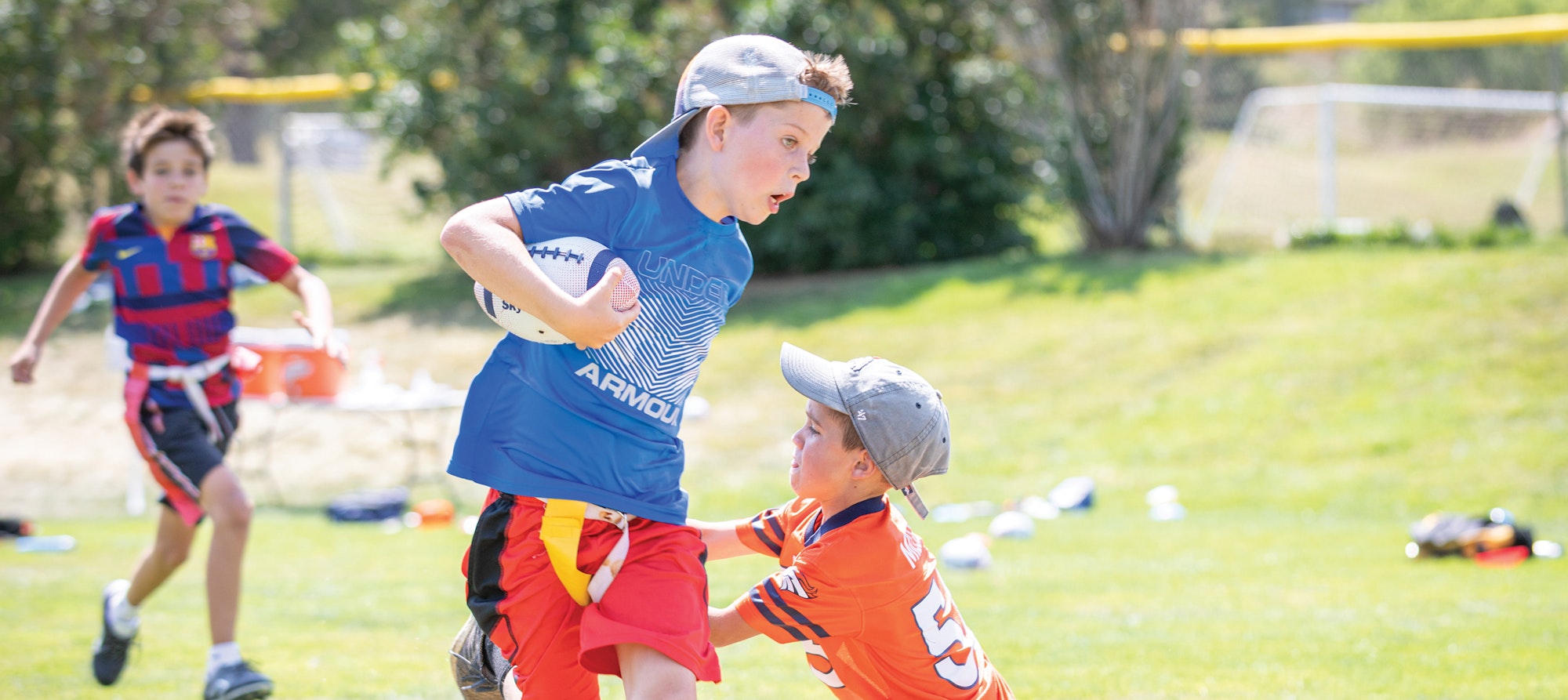 Kids playing flag football outdoors with one player evading a tackle.