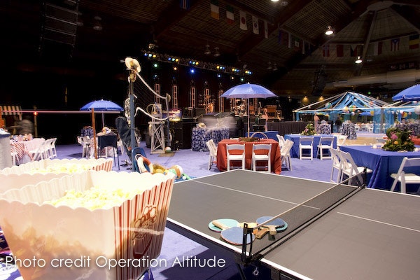 An indoor event space with a ping pong table, seating areas, popcorn, and a festive atmosphere.
