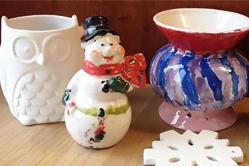 Three ceramic items: an owl, a snowman, and a painted pot, with a snowflake decoration in front.