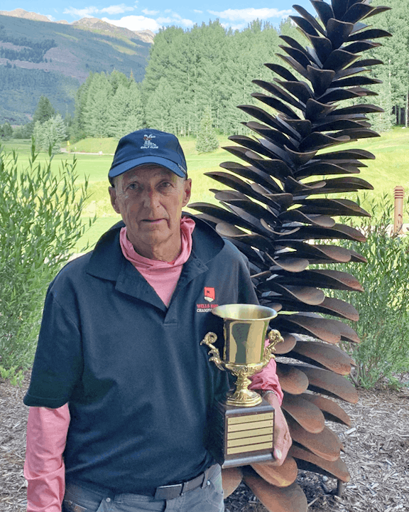 A man holding a trophy with a pine cone sculpture and a golf course in the background.