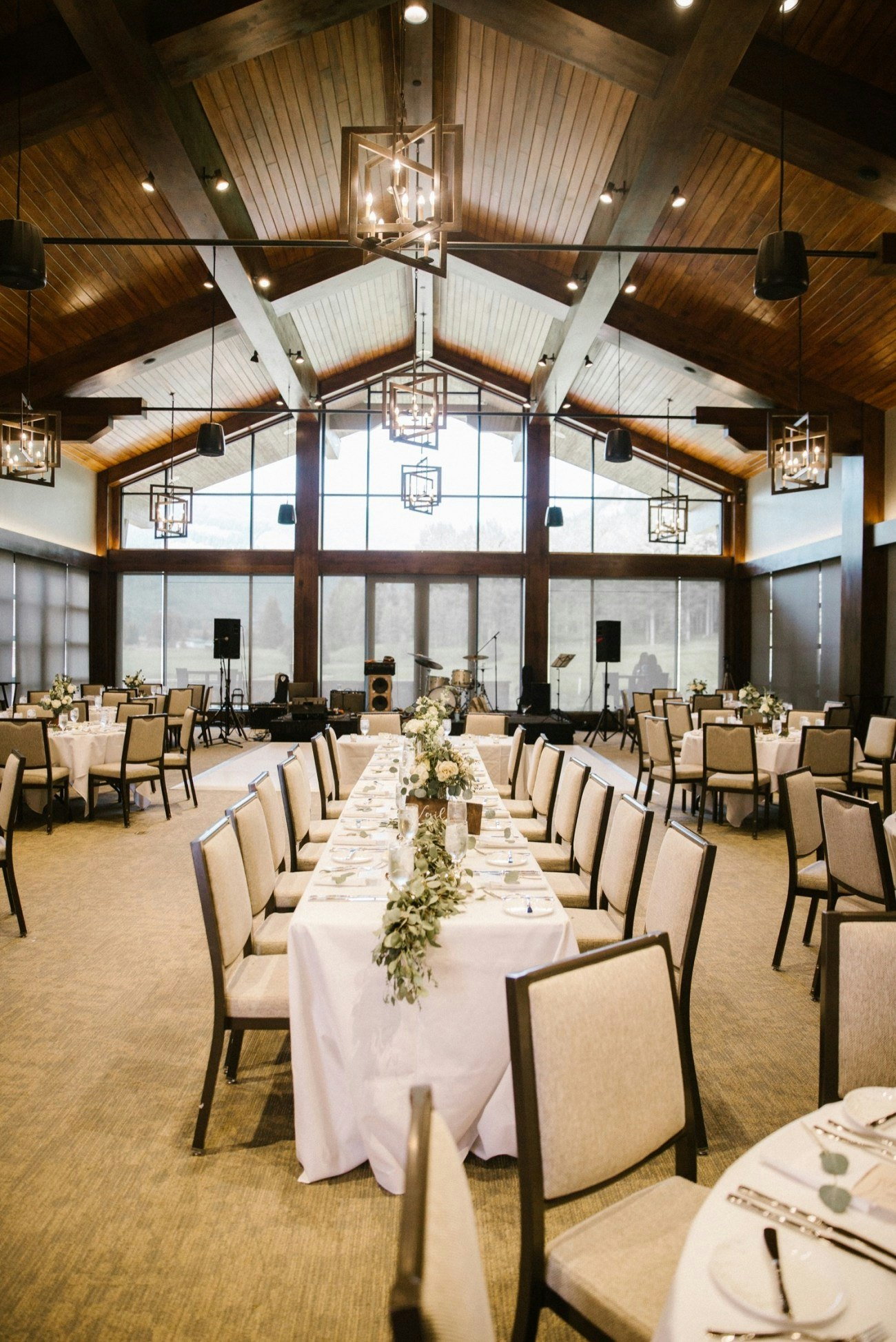 Elegant dining hall with a long table setup, wooden ceiling, and modern chandeliers.