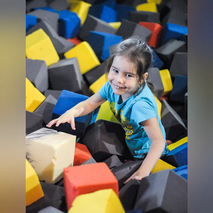 A smiling child in a foam pit with colorful blocks.