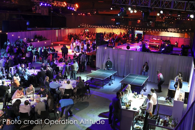 Event venue with people socializing, playing table tennis, and a stage in the background, with dimmed lighting and party ambiance.
