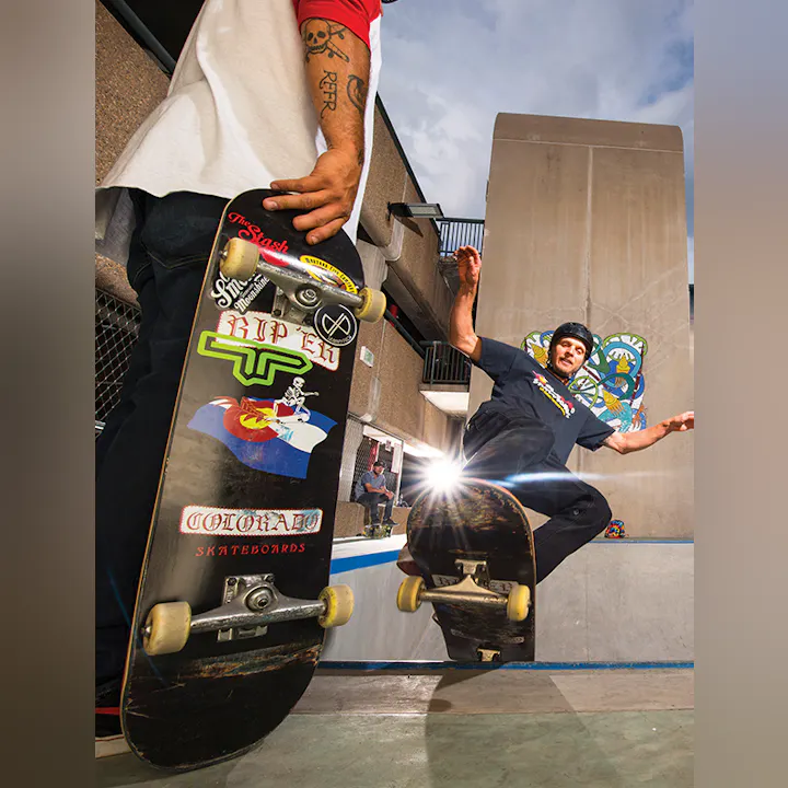 A skateboarder performing a trick, another person watching, and vibrant graffiti art in the background.