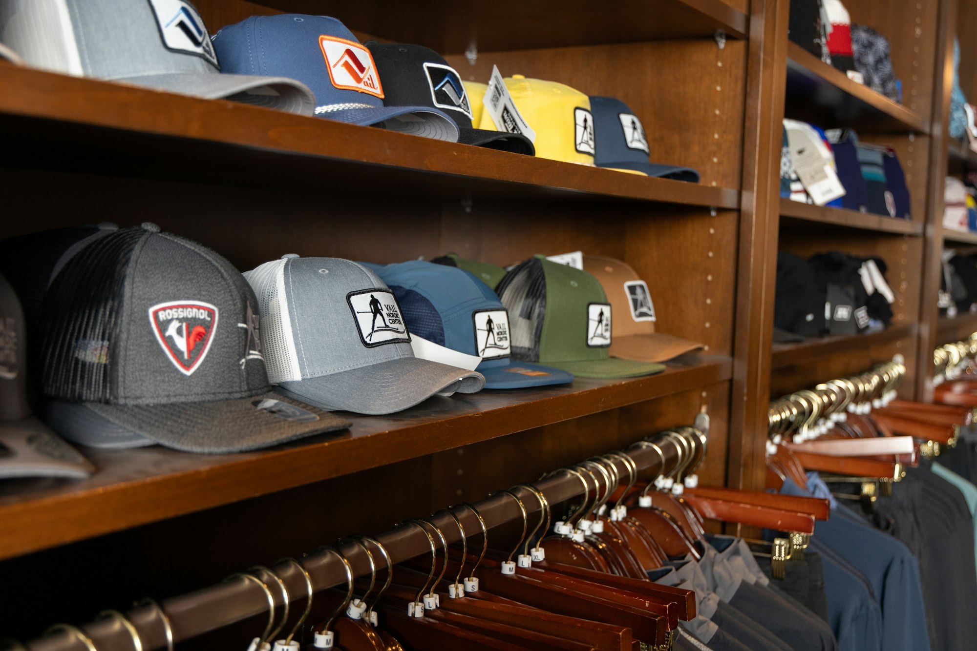 Hats and clothing on wooden shelves and hangers, displaying various designs and colors.