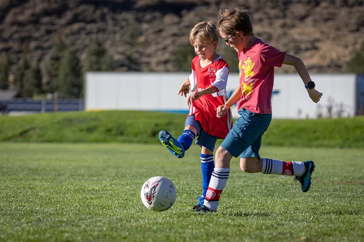 Two children playing soccer on a grassy field.