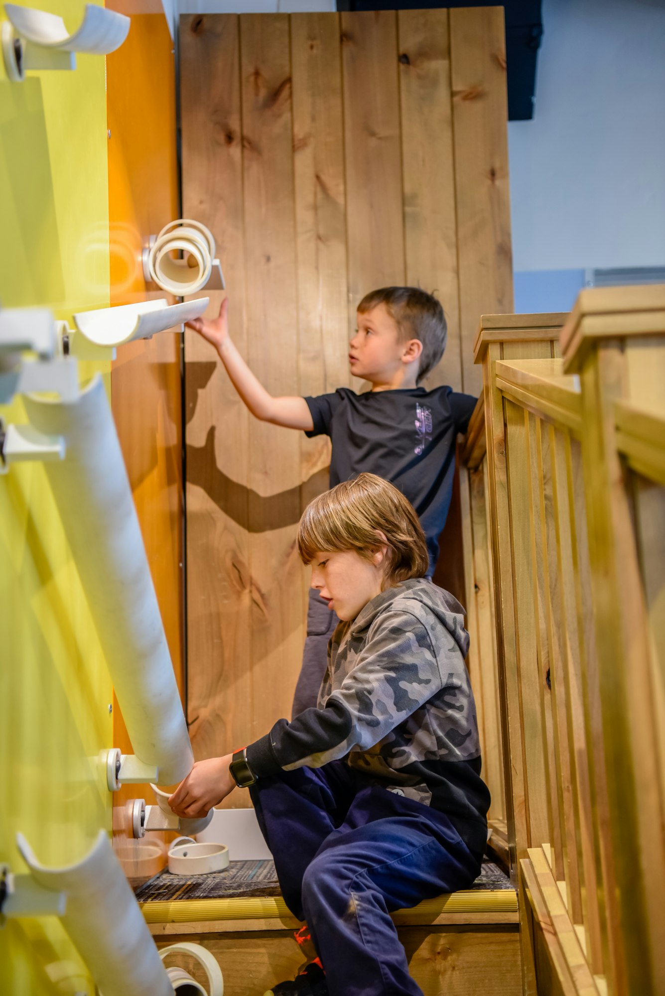Two kids engaged with a wall-mounted interactive exhibit, possibly in a museum or play area.