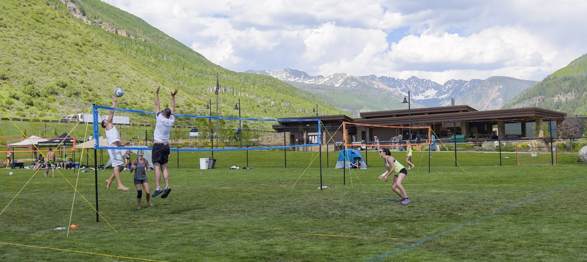 People playing volleyball outdoors with mountains in the background.