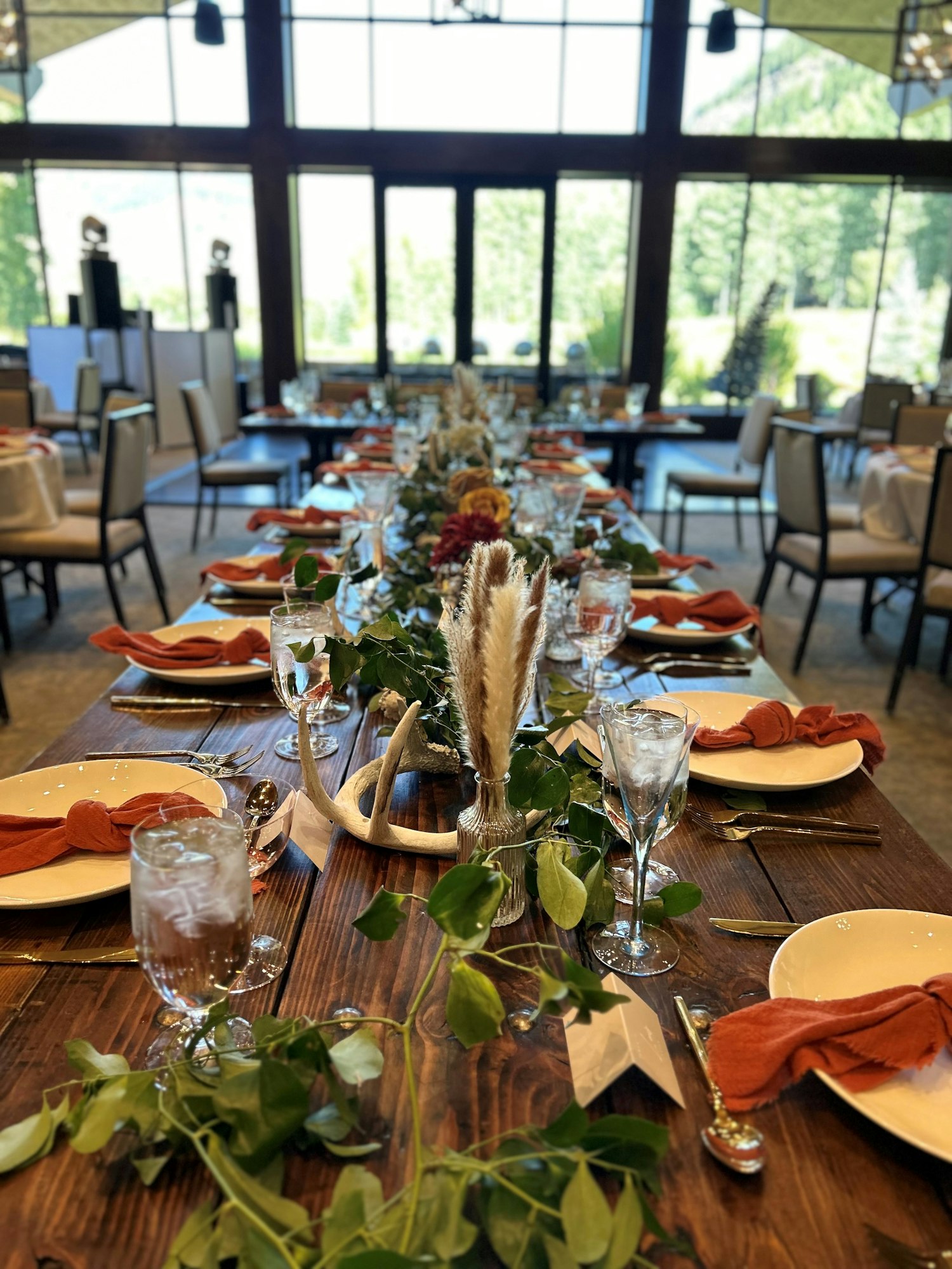 Elegantly set dining table with greenery, antlers, and rustic decor, ready for an event.
