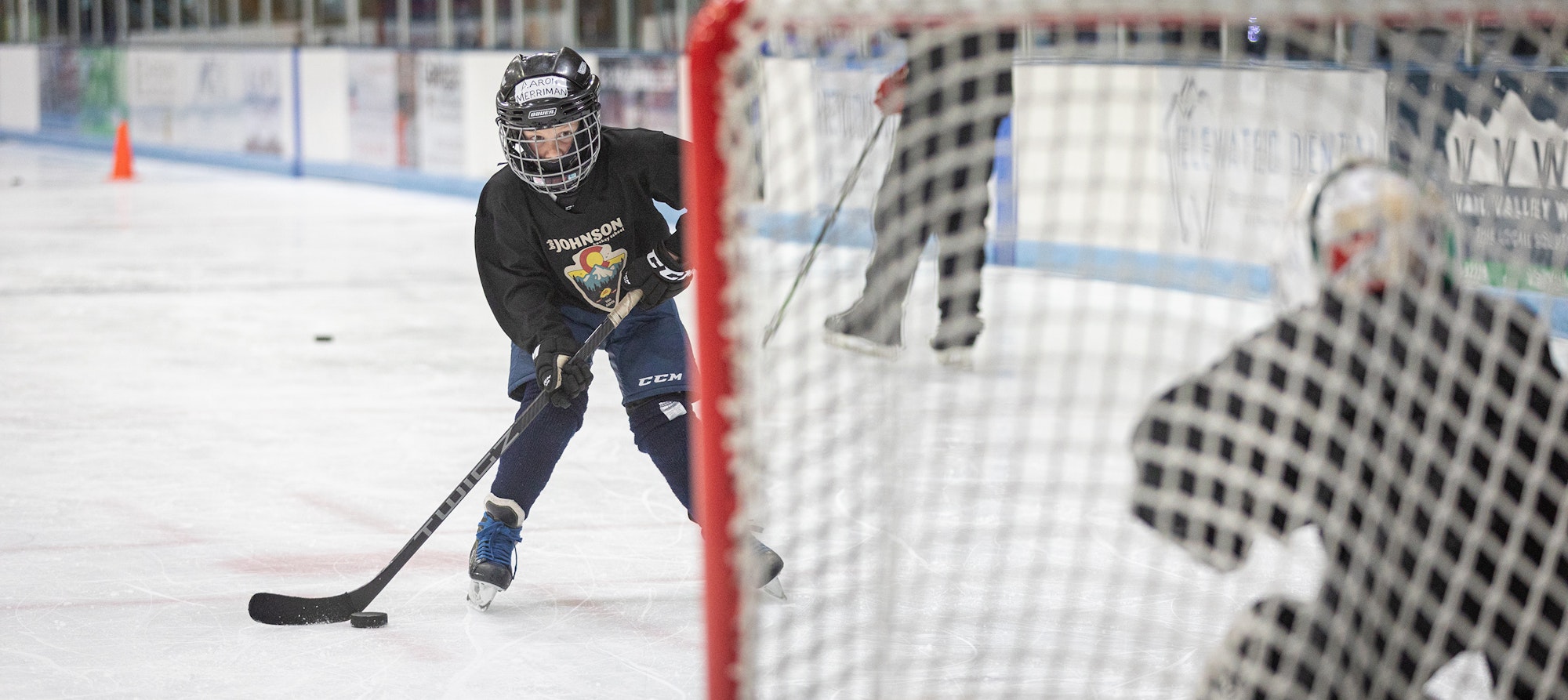 A hockey player on ice practicing a shot with a puck near the goal.