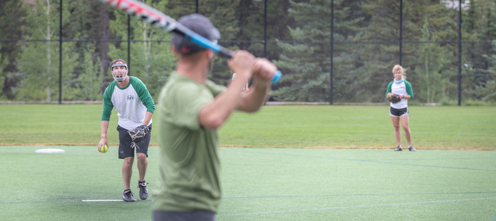 Three people playing softball, one batting, one pitching, and one fielding.