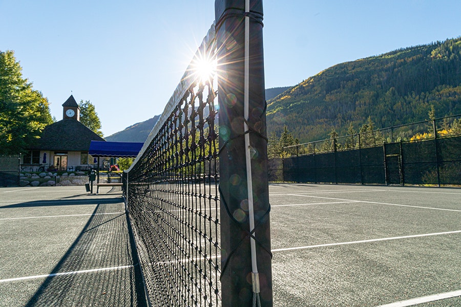 Tennis court net, sun flare, gazebo, mountains, clear sky.