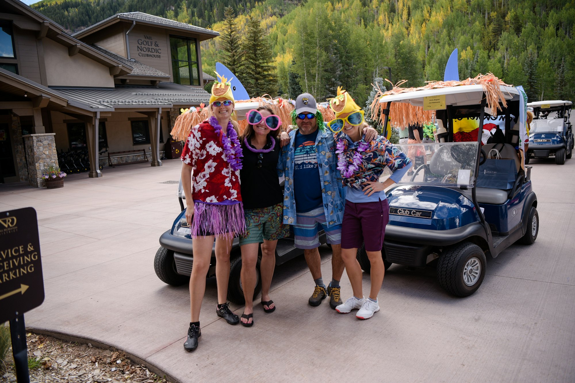Group of people in festive attire with a decorated golf cart at a clubhouse.