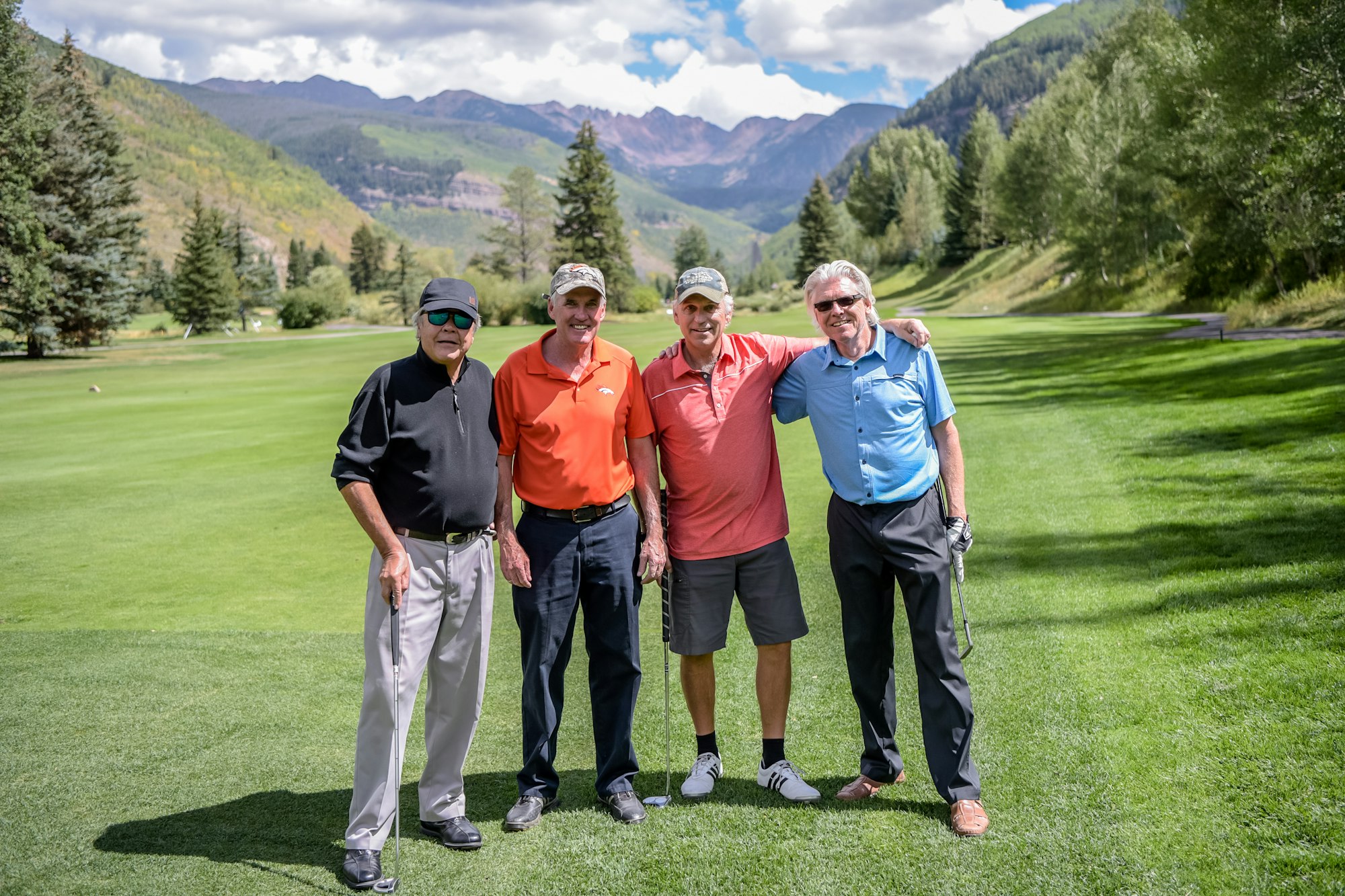 Four men posing on a golf course with a mountain backdrop.