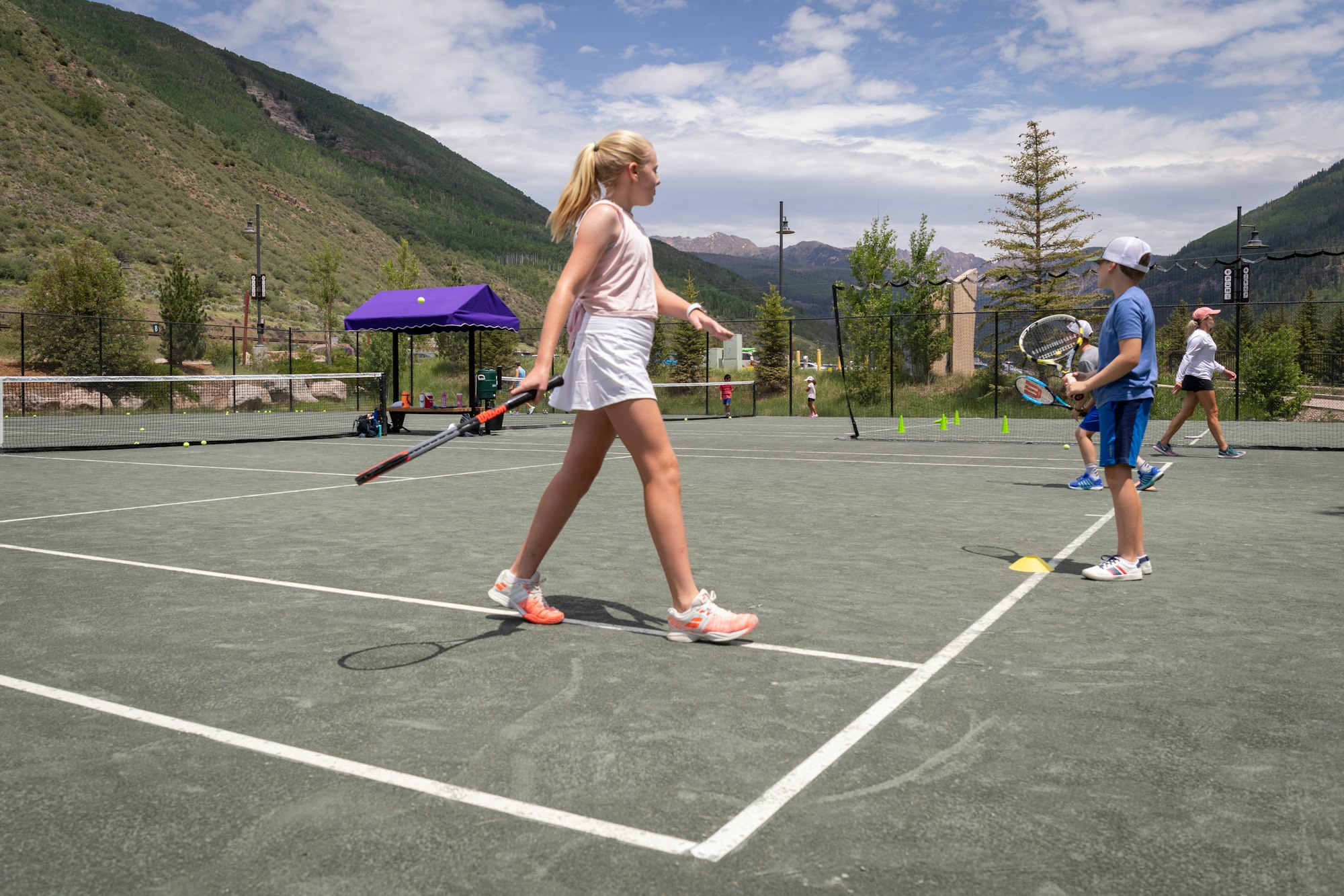 People playing tennis on an outdoor court with mountains in the background.