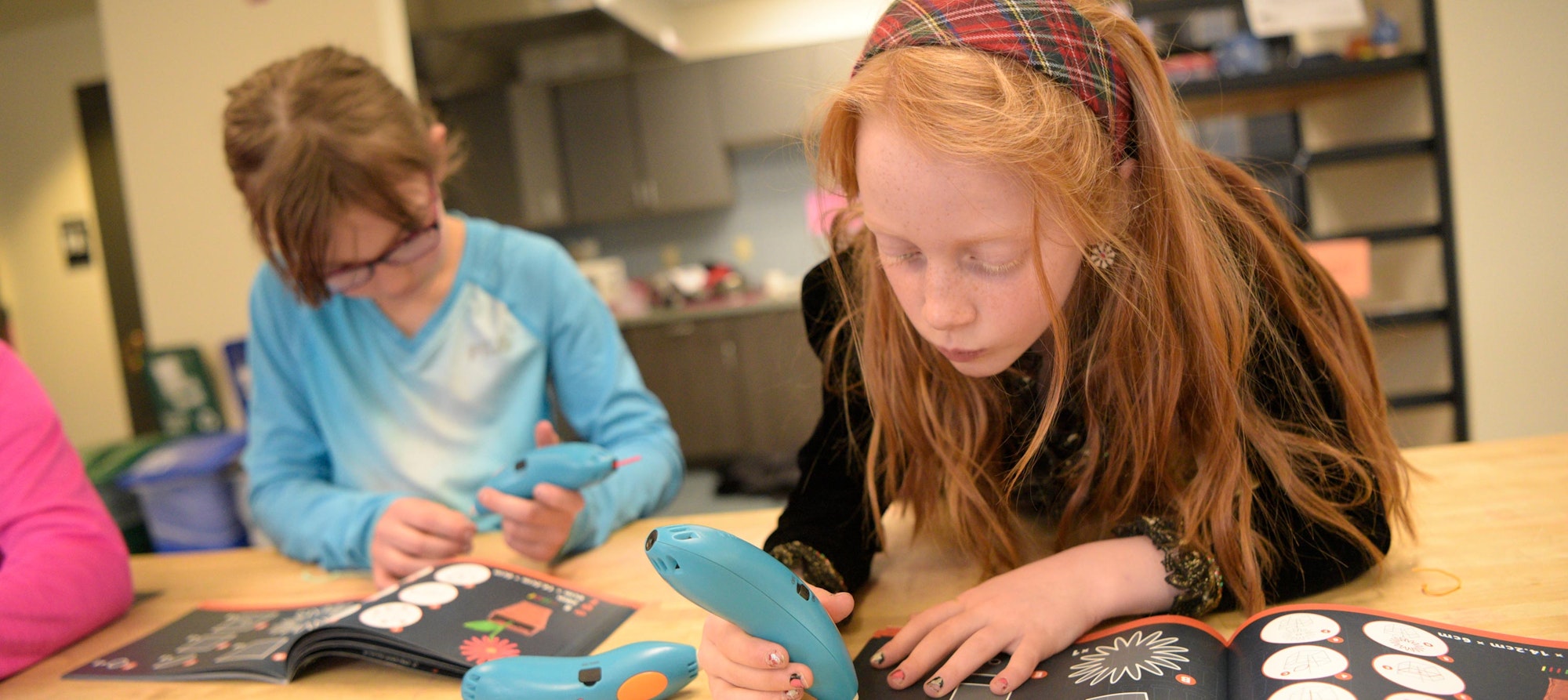 Two kids engaging in a creative activity with electronic devices and a craft book.
